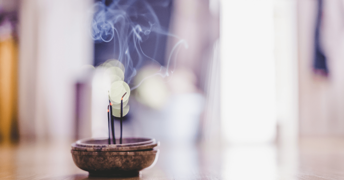 A scent stick in a bowl lit and producing smoke.