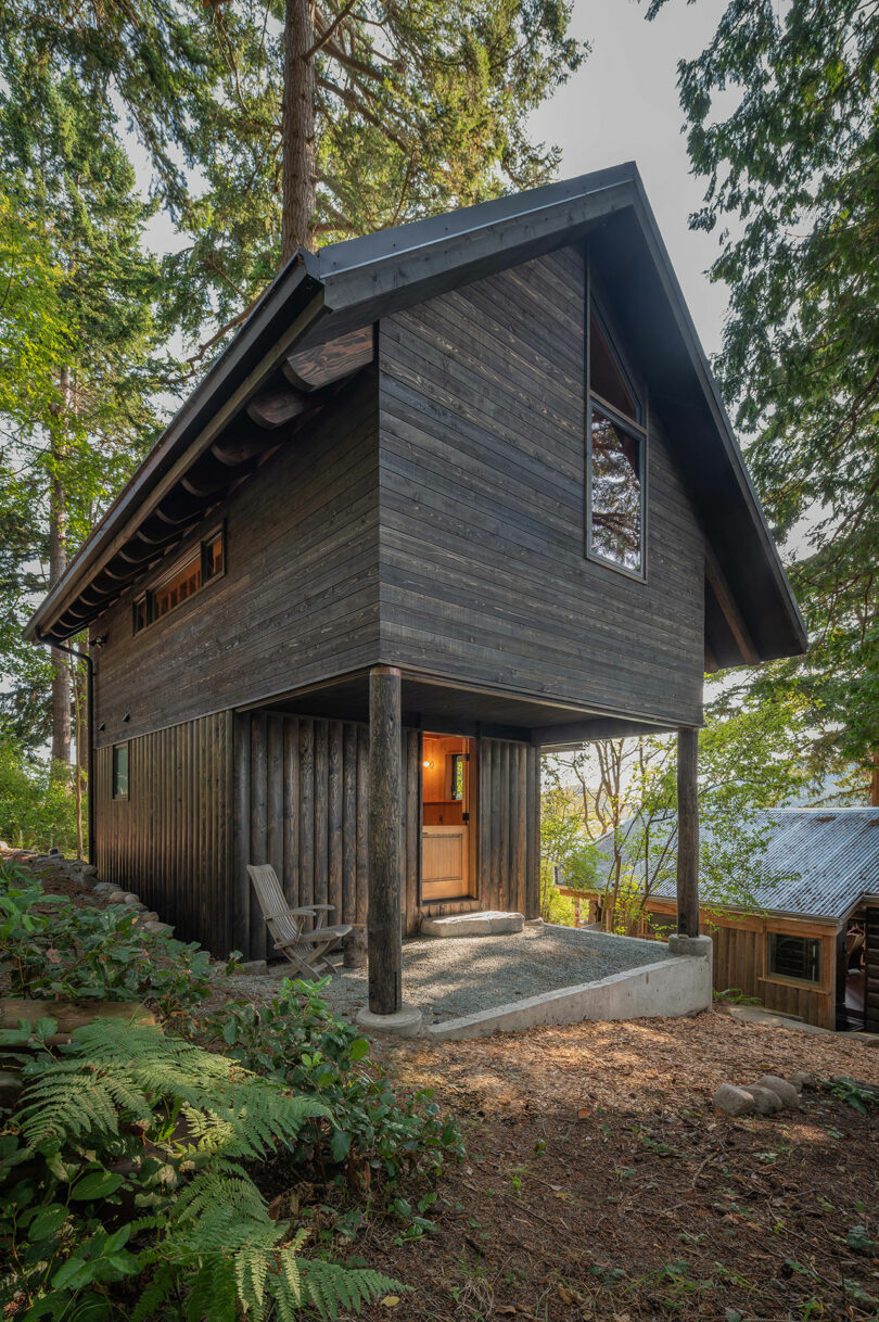 corner exterior view of black two-story narrow cabin in woods