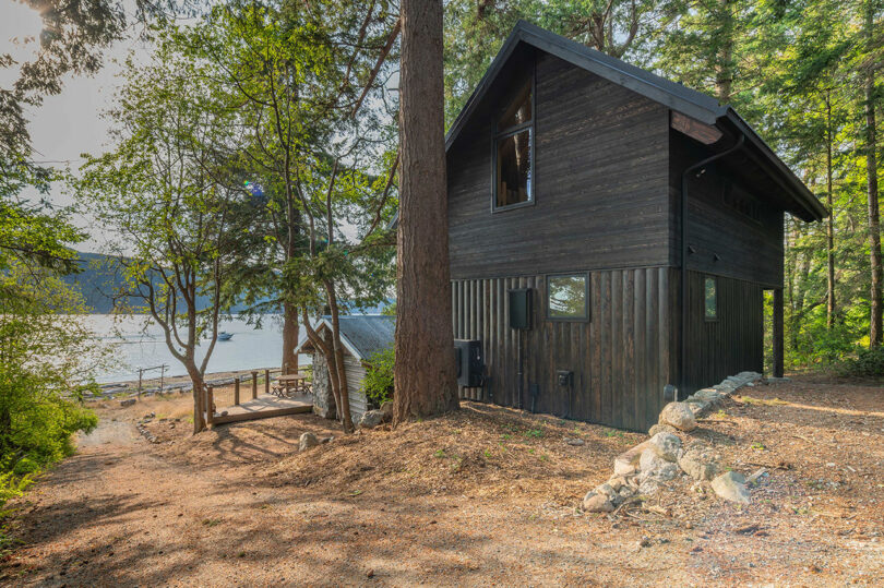 back angled exterior view of black two-story narrow cabin in woods