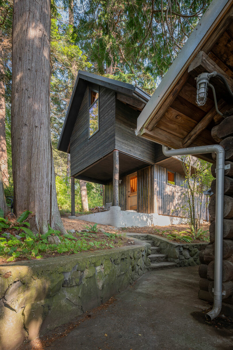 down slope exterior view of black two-story narrow cabin in woods