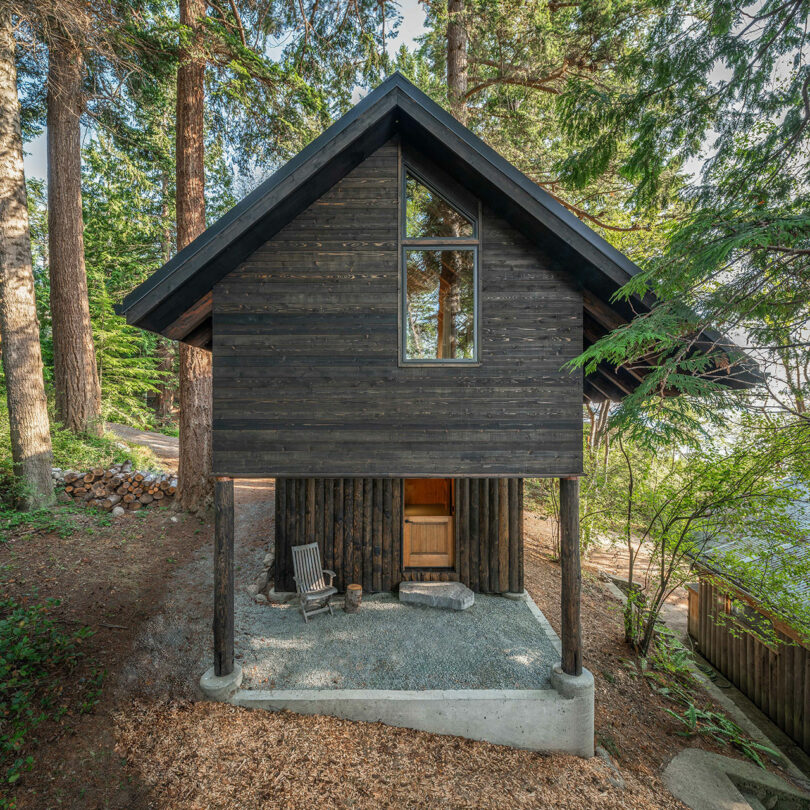 front exterior view of black two-story narrow cabin in woods
