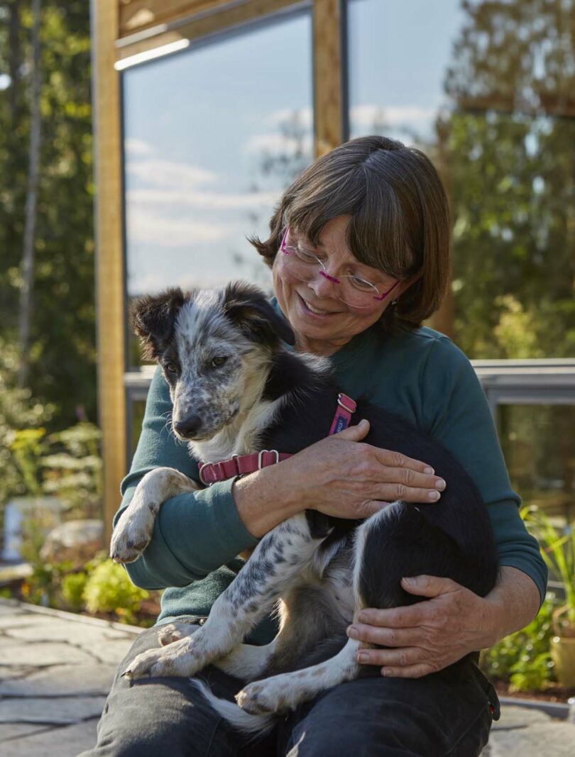 A woman sitting outdoors holding a small dog in her lap.