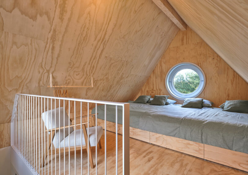 A room with a round window and large bed under wood pitched roof.