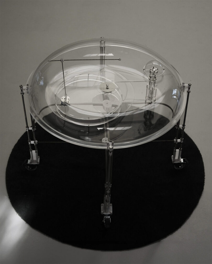 Glass vacuum chambered circular table designed to resemble scientific equipment containing water fountain and dowsing rod
