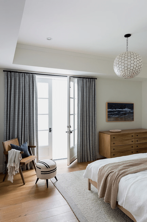 Gray curtains cover French doors located behind a vintage cane chair placed in a corner with a black and white round stool.