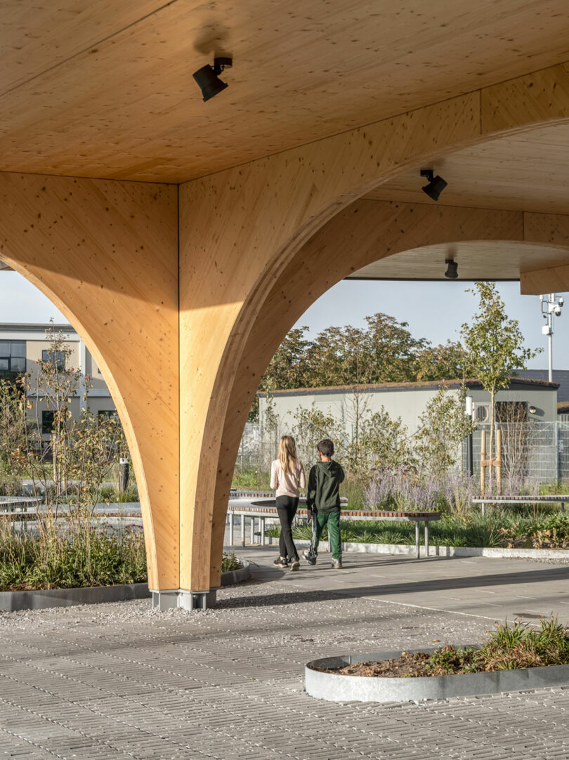 A wooden structure with people walking underneath it in the park.