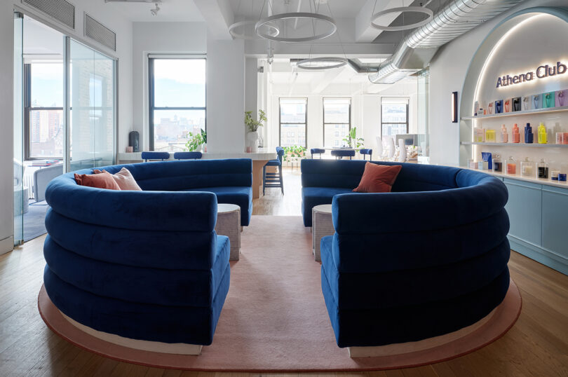 Two semi-circular shaped blue couches in a room with lots of windows.