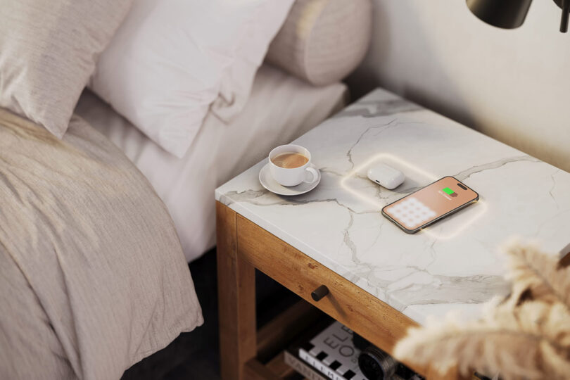 A bedside table with a phone and a cup of coffee, featuring wireless charging through the stone countertop surface.