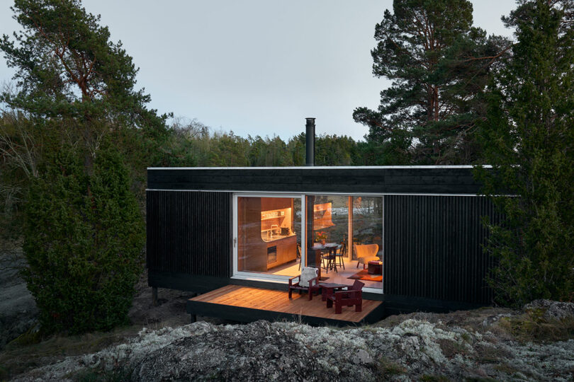 Modern cabin with large windows nestled in a forest at dusk.