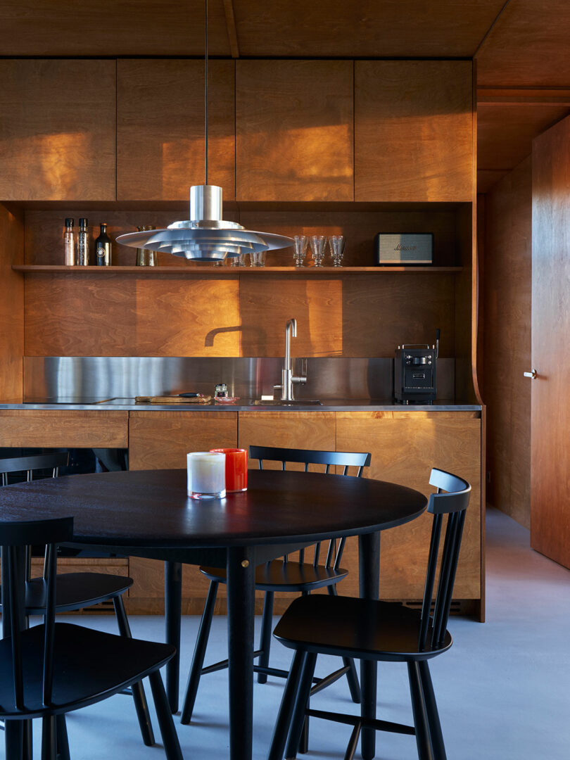 Modern kitchen with wooden cabinetry, stainless steel countertop, and a black dining set.