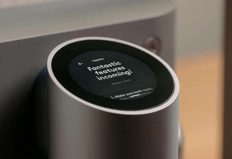An AI-enhanced coffee machine with a message on it communicating an incoming software update with "Fantastic features incoming!" on a circular display
