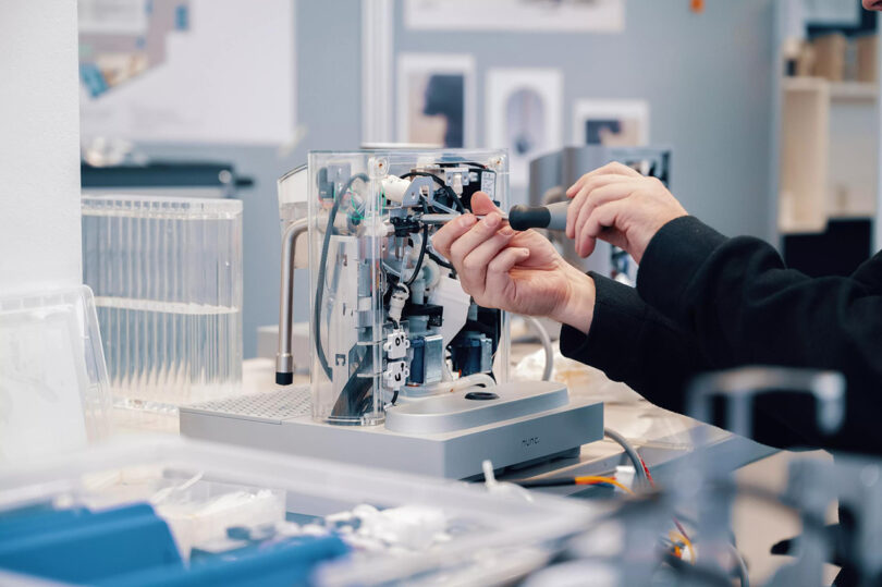 A man working on assembling the nunc. an AI-enhanced coffee machine in a lab/factory setting.