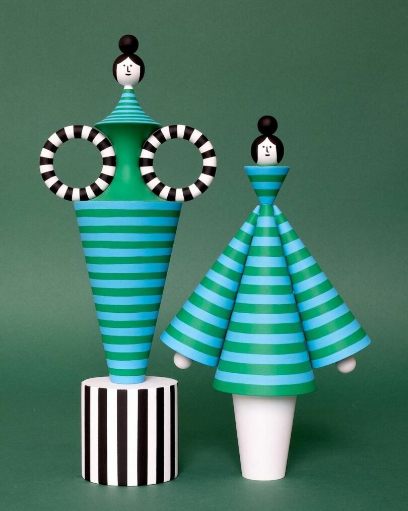 two wooden sculptures of women wearing striped outfits and a top knot