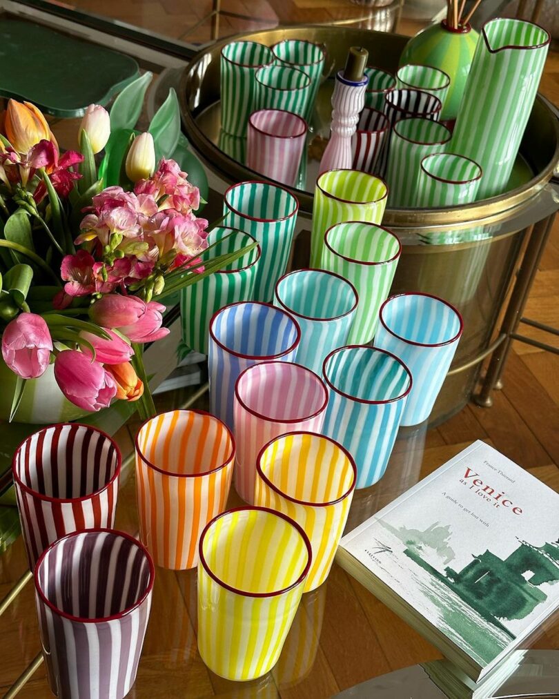 a rainbow of stripe drinking glasses on a table with flowers and a magazine