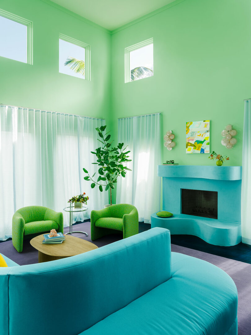 A vibrant living room with a blue fireplace, green furniture, light green walls, and sheer curtains.