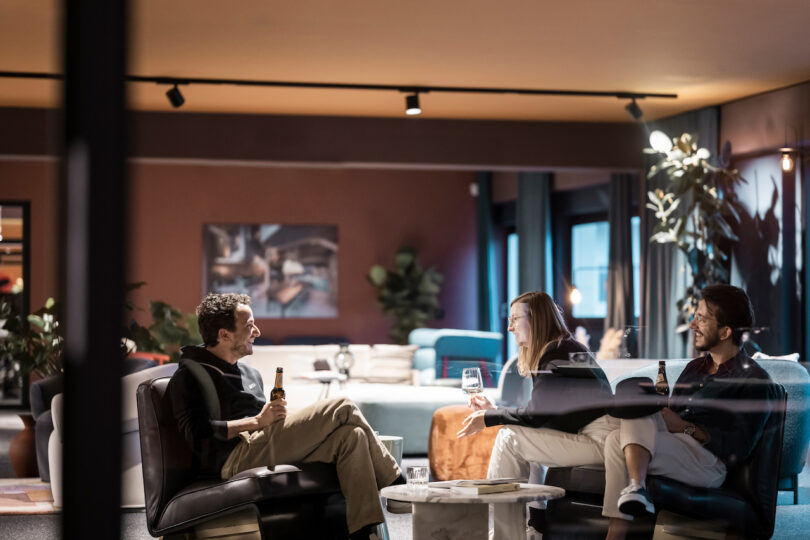 Three people enjoying a relaxed conversation with drinks in a stylish NOA lounge area.