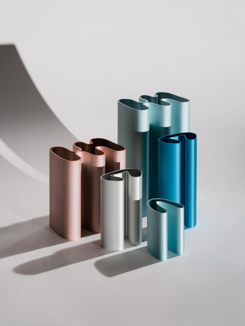 A collection of cylindrical, rolled metal sheets in various colors including teal, blue, and copper, arranged on a white surface with shadows.