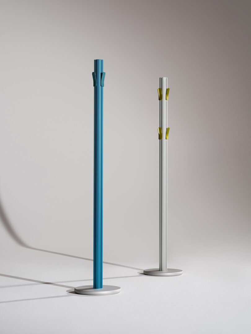 Two modern, minimalist coat racks, one blue and one silver, against a light grey background.