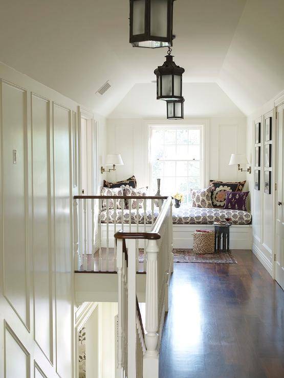 Staircase landing features a reading nook with built in window seat bench accented with a block print black and white cushion lit by white shaded sconces and a gray Moroccan accent table atop a vintage rug.