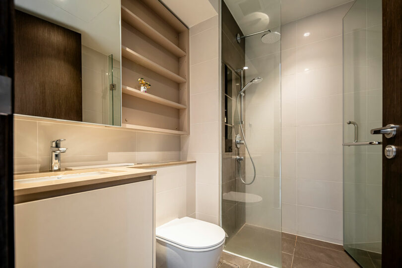 Modern bathroom interior with a glass shower, wooden cabinets, and beige tiles.