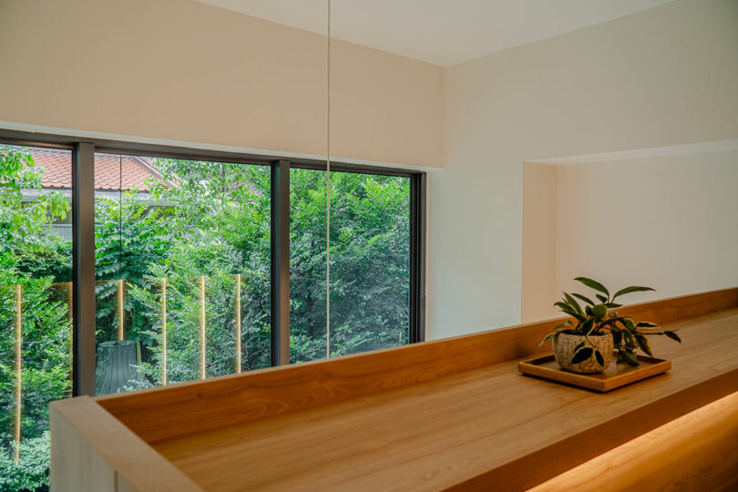 A serene interior featuring a wooden ledge by large windows overlooking lush greenery, with a small potted plant as decoration.