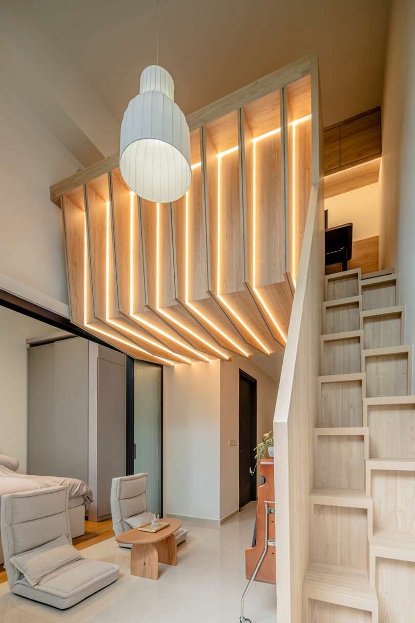 Modern interior of a home featuring a unique wooden ceiling design with embedded lighting, a staircase, and minimalist furnishings.