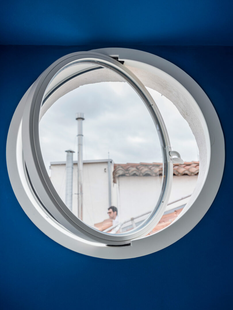 Circular window partially open surrounded by a bright blue wall