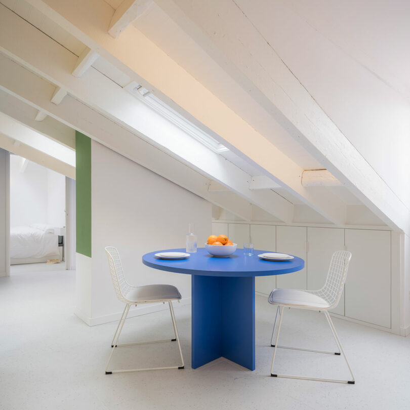 Minimalist attic dining area with white decor, a blue round table, and modern chairs.
