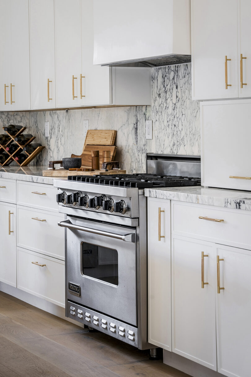 Modern kitchen with white cabinetry, gold handles, marble backsplash, and a stainless steel stove.