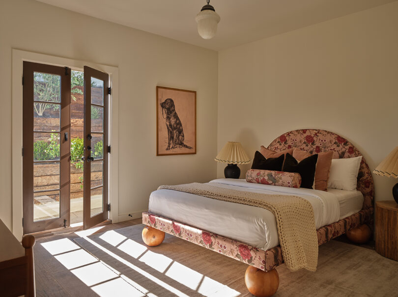 Cozy bedroom with a floral-patterned bed, wooden furniture, and an open door leading to a sunlit patio.