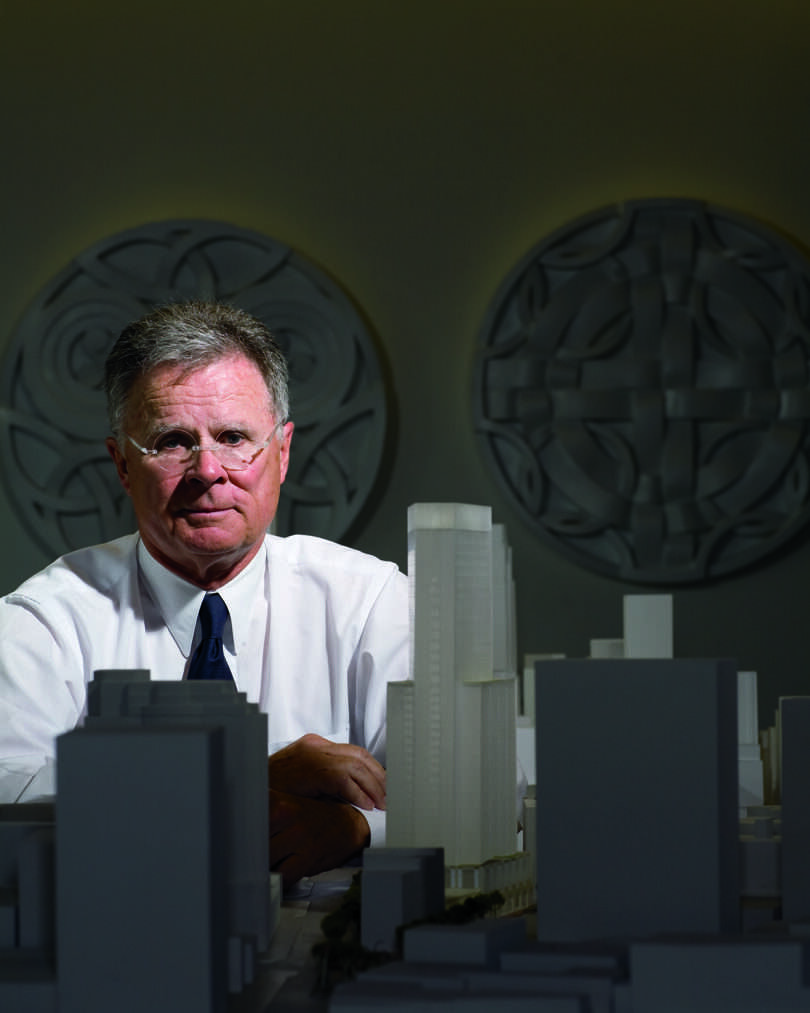 Man in a white shirt standing behind an architectural model of a building complex.
