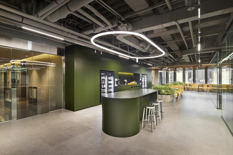 Modern office kitchenette with a circular overhead light fixture, a curved bar, and an exposed ceiling.