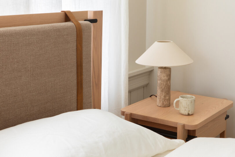 A neatly made bed with a wooden headboard and a nightstand featuring a lamp and a cup.