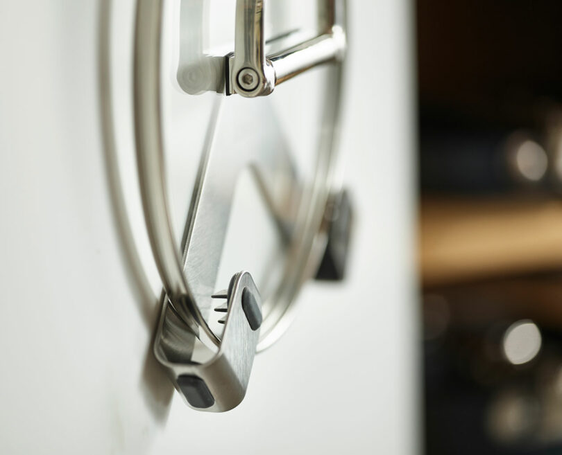 A close-up of metal pot lids hanging on a kitchen rack, with focus on the front lid's handle.