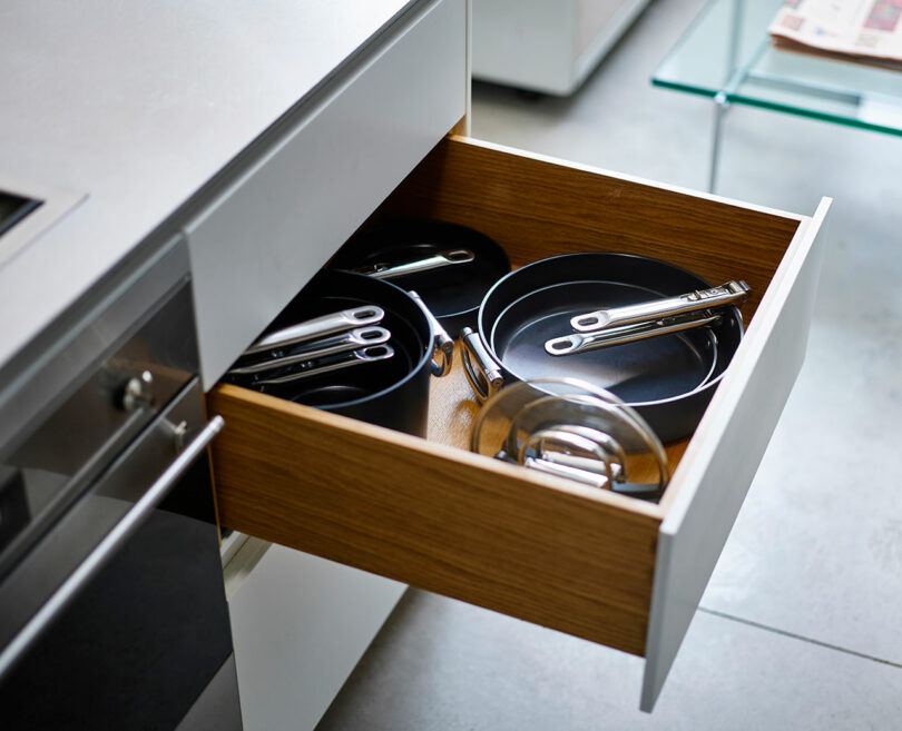 A kitchen drawer partially opened containing neatly arranged pots and lids.