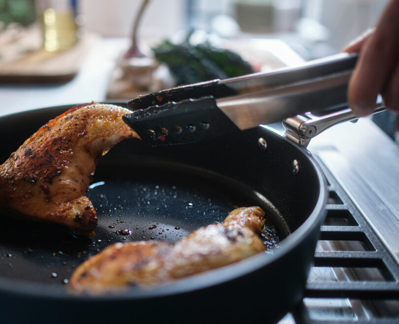 Cooking chicken breasts in a frying pan with tongs.