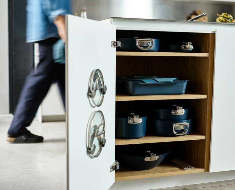 A kitchen cabinet with open shelves, neatly stacked with various sizes of pots and pans.