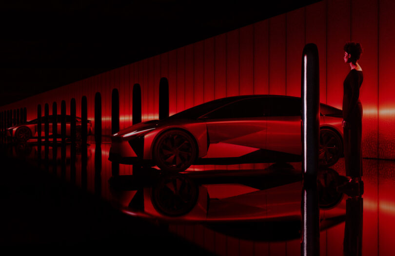 Woman standing next to a sleek red Lexus sports car in a dimly lit, futuristic garage with reflective floors and illuminated columns.