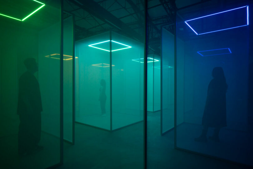 Silhouettes of two people in a foggy, neon-lit room filled with mirrors and geometric light fixtures.