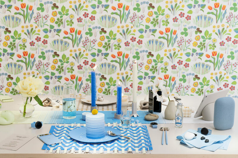 A festive dining table setup with blue and white tableware, floral wallpaper in the background, and a variety of decorative objects.