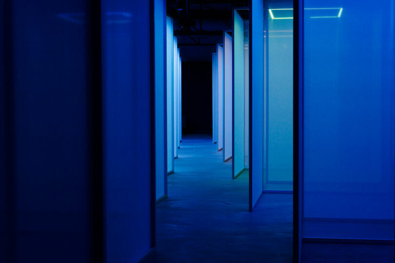A dimly lit corridor with blue neon lights and open doorways, creating a futuristic ambiance.