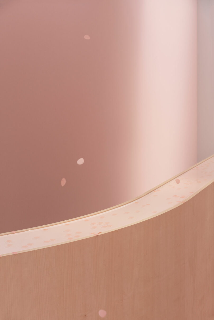 Curved wooden counter with a speckled surface against a soft pink curved wall in a minimalist interior design.