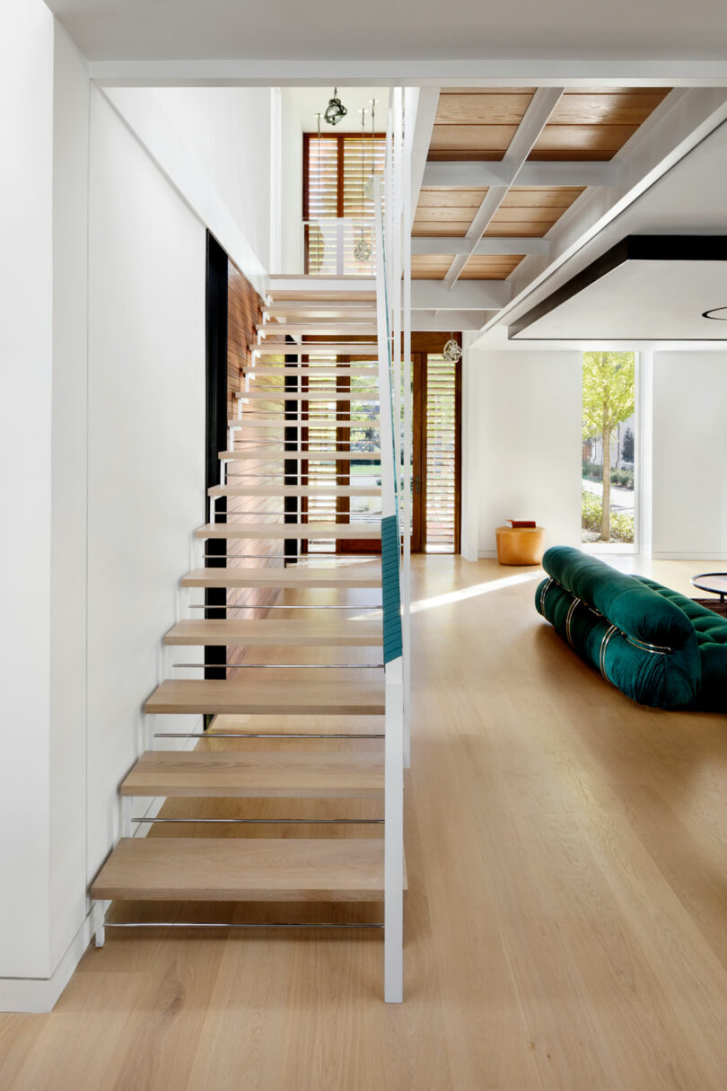 Modern interior showcasing wooden stairs with metal railing, leading to an upper floor in a bright, open-plan house.