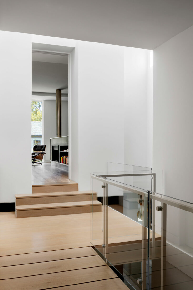 Modern interior with clean lines featuring wooden steps and a glass balustrade leading to an adjoining room.