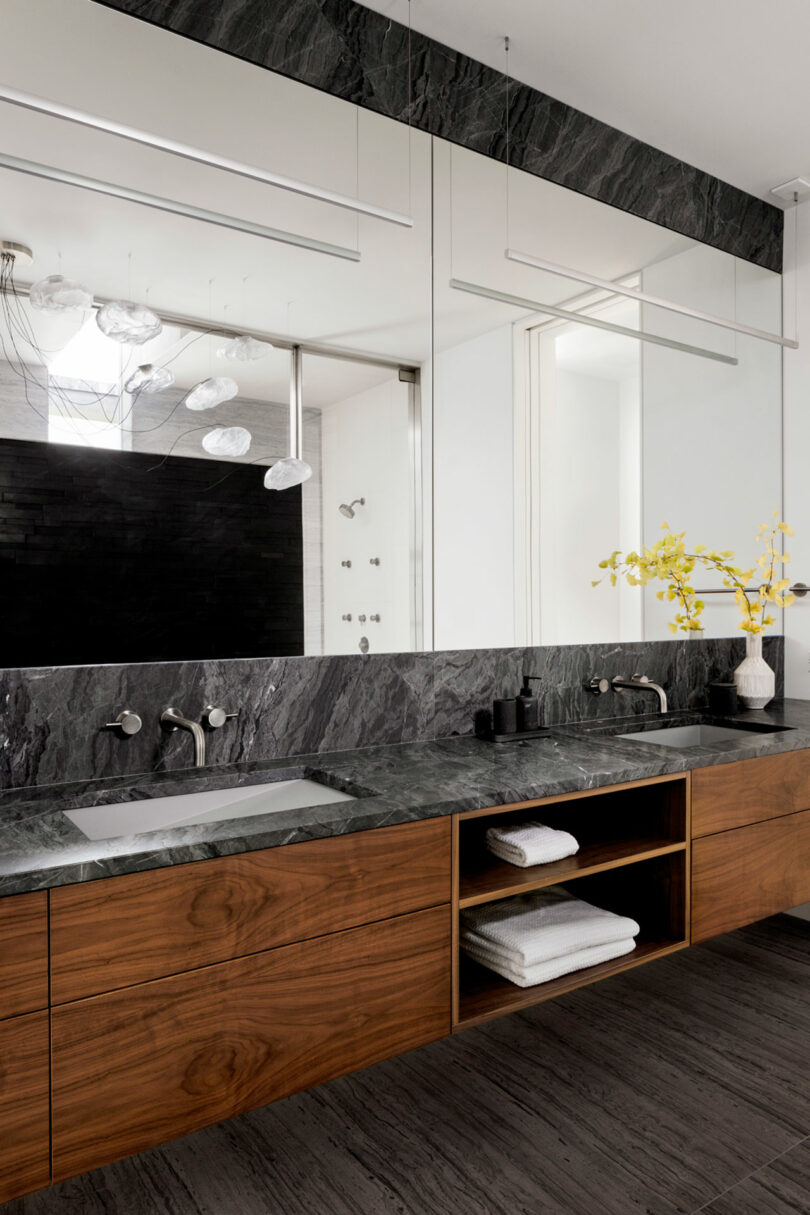 angled view of modern bathroom with double sink vanity with grey and white marble tops and dark wood cabinets