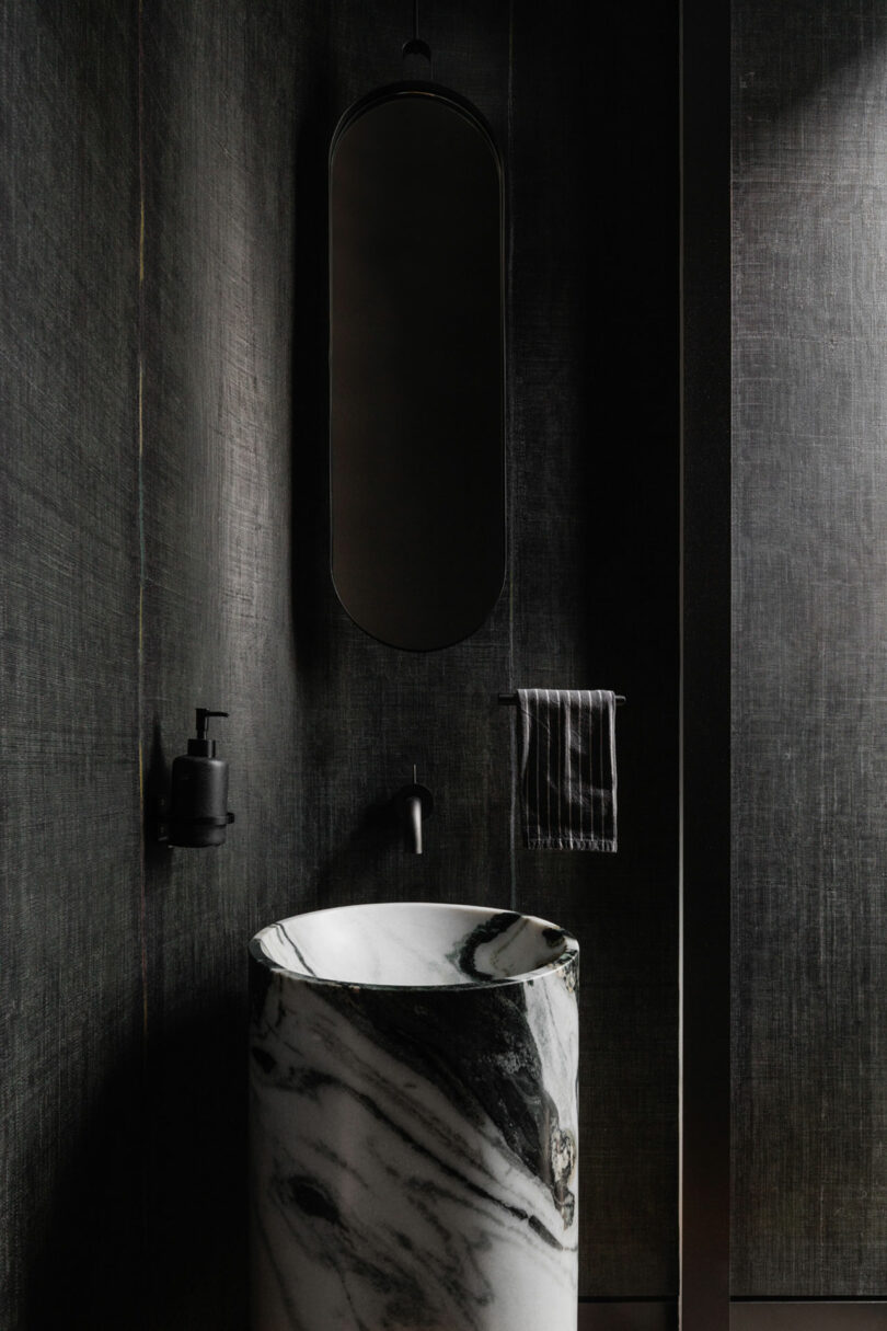 Dark, black bathroom with solid cylindrical black and white marble sink