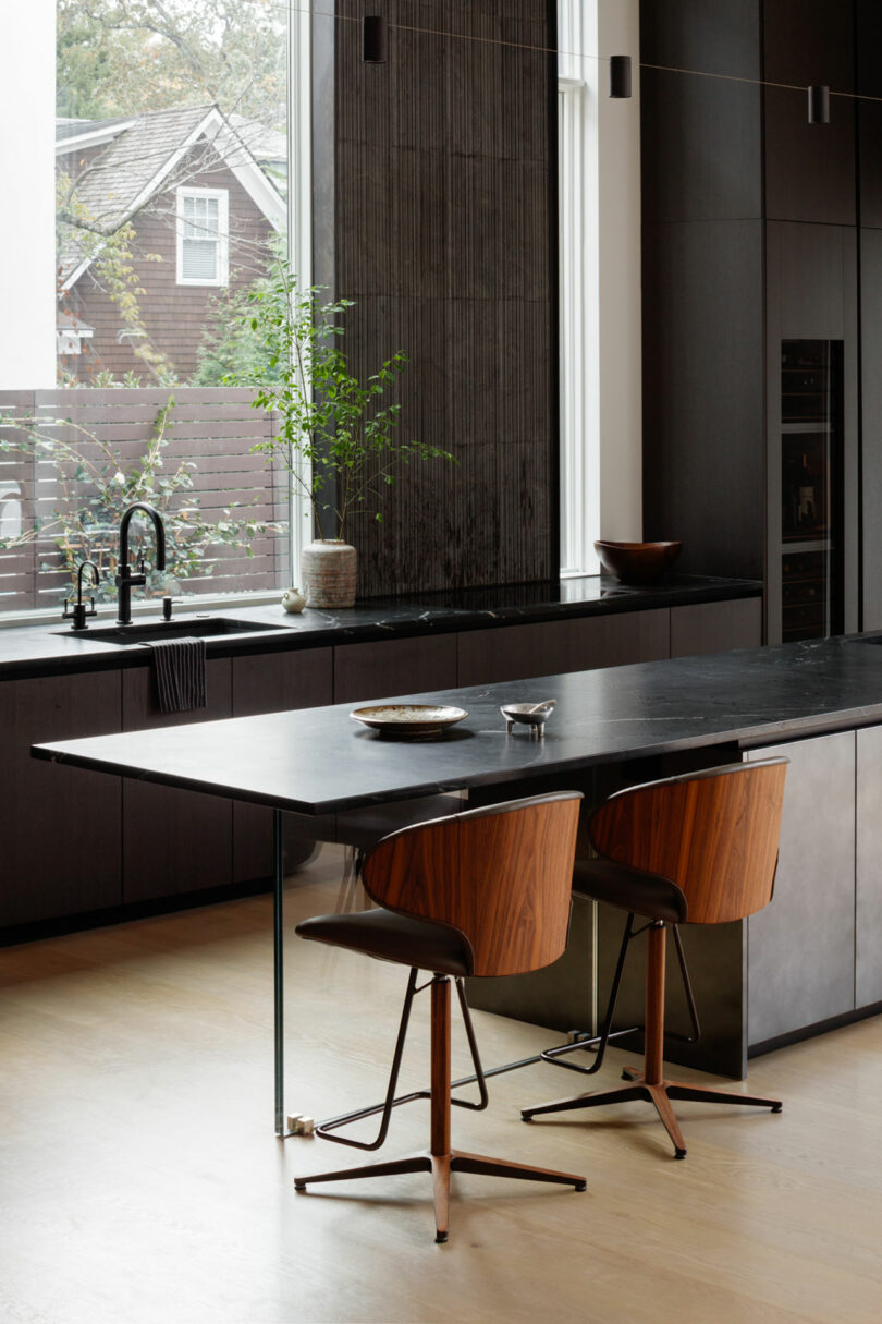 Modern kitchen interior with dark cabinetry and a central island featuring a stone countertop and wooden stools.