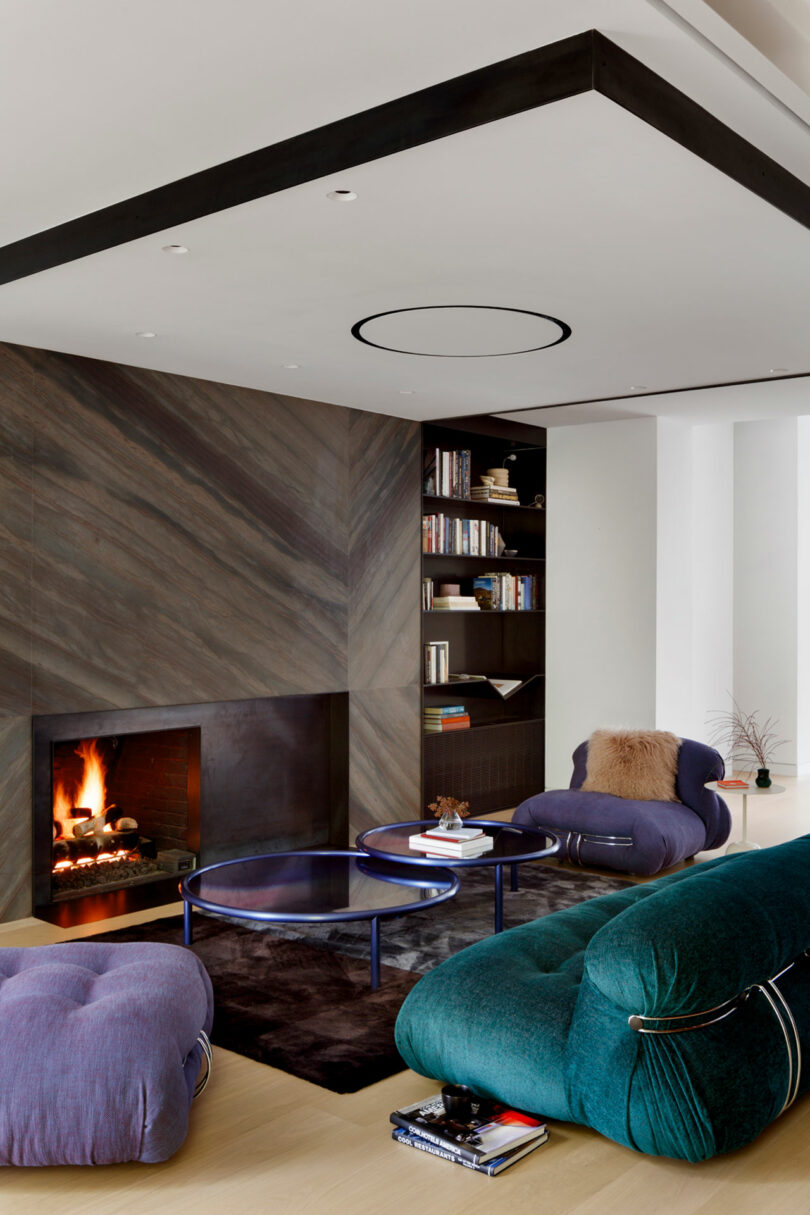 Modern living room with a dark marble fireplace, teal sofa, circular coffee tables, and built-in bookshelf.