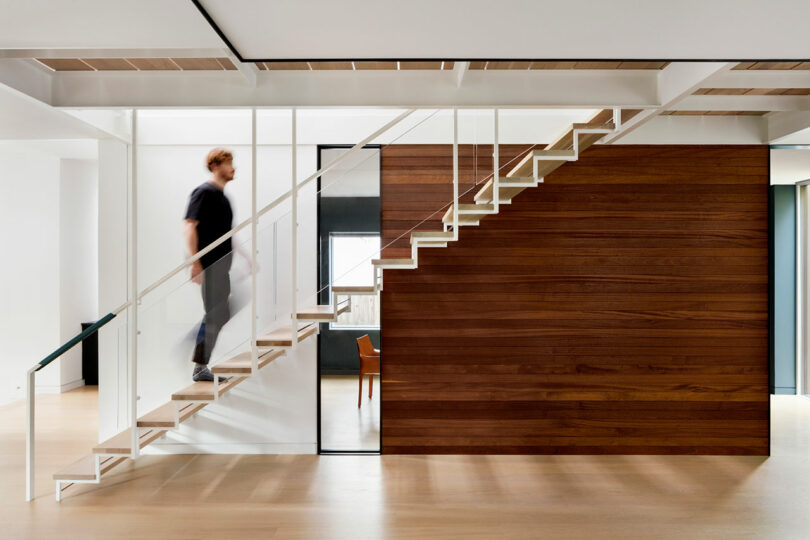 A person ascends a modern staircase with wooden steps in a bright, minimalistic interior.