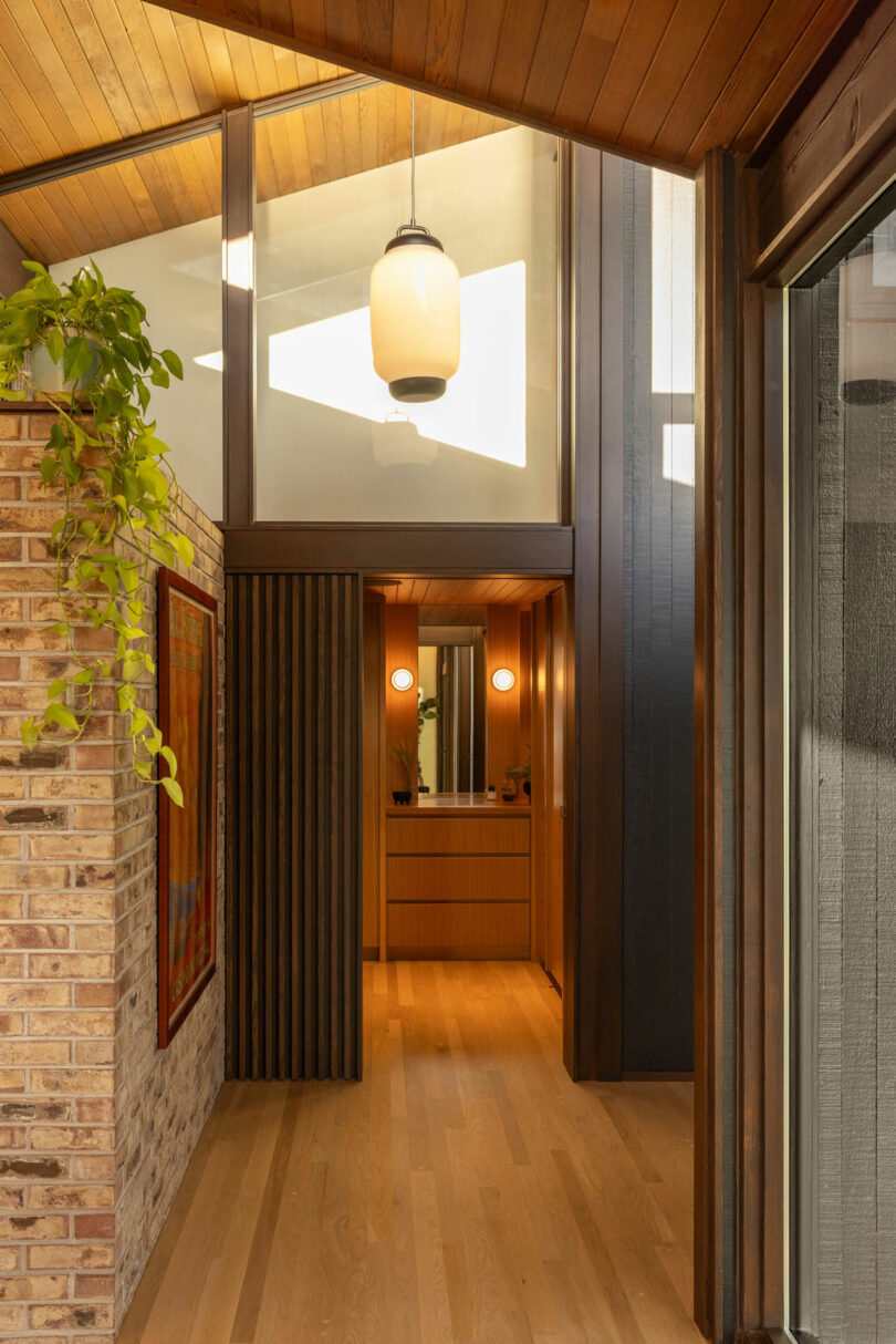 Modern home interior featuring a warm, well-lit foyer with wooden floors, exposed brick wall, and a pendant light, seen from the entrance.